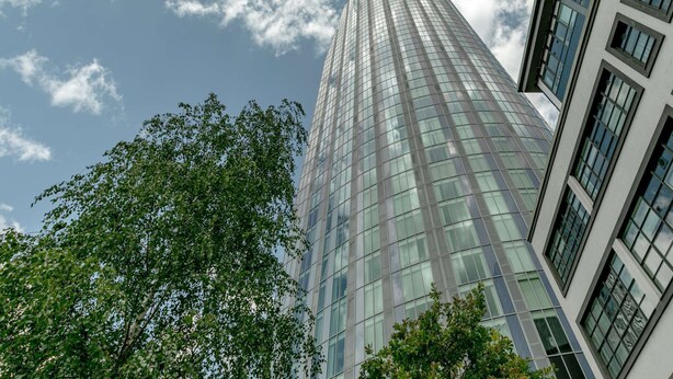 A tall, modern glass building with a grid-like facade, surrounded by trees. - Modern 1-Bedroom Stay in Stratford near to Canary Wharf | Ideal for Business or Leisure (London)