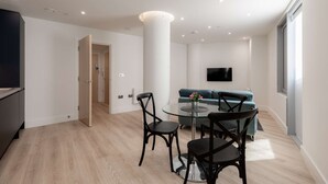 A modern living room with a glass dining table, black chairs, a teal sofa, and a flat-screen TV mounted on the wall. - Modern 1-Bedroom Stay in Stratford near to Canary Wharf | Ideal for Business or Leisure (London)