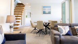 Una sala de estar moderna con un sofá, una mesa de comedor con sillas, una lámpara y una escalera que conduce a otra habitación.