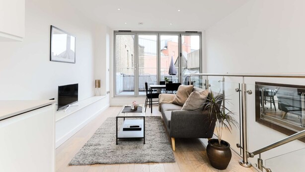 A modern living room with a sofa, coffee table, and TV. There is a balcony with a table and chairs. - Prime Serviced Apartments in Trafalgar Square, London (London)