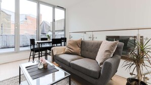 A modern living room with a grey sofa, a glass coffee table, and a dining area with chairs and a table. - Prime Serviced Apartments in Trafalgar Square, London (London)