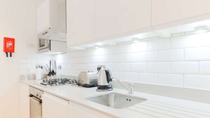 Une cuisine moderne avec des meubles blancs, un évier en acier inoxydable, une bouilloire et un grille-pain.