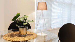 Une table en verre, surmontée d’un set de table en fibres tressées, agrémentée d’une plante en pot et d’un lampadaire.