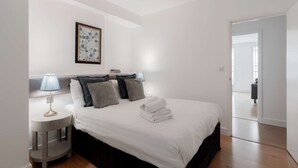 A bedroom with a bed, bedside lamps, a framed artwork, and a view into another room. - Premium Serviced Apartments in Covent Garden (London)