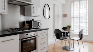 A modern kitchen with a gas stove, oven, and microwave. There is a dining area with a round table and black chairs. - Premium Serviced Apartments in Covent Garden (London)