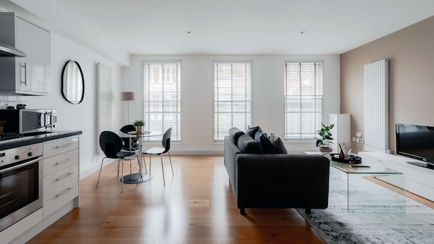 A modern apartment with a kitchen, dining area, and living room. It features large windows, a flat-screen TV, and a sofa. - Premium Serviced Apartments in Covent Garden (London)