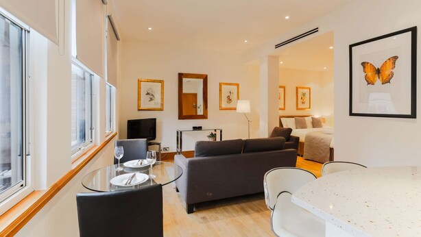 Une chambre d’hôtel moderne avec une table à manger en verre, un canapé, un lit et des œuvres d’art accrochées aux murs.