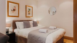Une chambre d’hôtel bien rangée, avec un lit, des tables de chevet et deux reproductions encadrées de motifs botaniques accrochées au mur.
