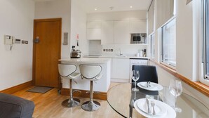 Une cuisine moderne avec des meubles blancs, un four en acier inoxydable et une table à manger en verre, accompagnée de chaises.