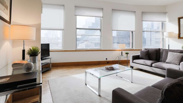 A modern living room with a glass coffee table, grey sofa, and a TV on a stand. - Monument by Excel Apartments, London – Perfect for Short Lets and Corporate Stays (London)