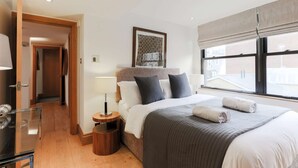 A modern hotel room with a large bed, a bedside table, a lamp, and a window with a view of buildings. - Monument by Excel Apartments, London – Perfect for Short Lets and Corporate Stays (London)