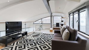 A spacious living area with a large flat-screen TV, a modern sofa, and a patterned rug. - Monument by Excel Apartments, London – Perfect for Short Lets and Corporate Stays (London)