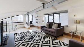 A modern living room with a grey sofa, a patterned rug, and a glass coffee table. - Monument by Excel Apartments, London – Perfect for Short Lets and Corporate Stays (London)
