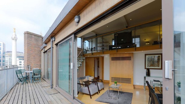 A modern apartment with a balcony, a living area with a sofa and coffee table, and a staircase leading to an upper floor. - Monument by Excel Apartments, London – Perfect for Short Lets and Corporate Stays (London)