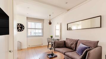 Een moderne woonkamer met een bruine leren bank, een ronde houten salontafel en een grote spiegel aan de muur.
