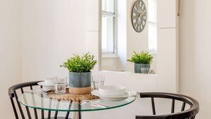 Un coin repas avec une table en verre, deux chaises noires, une plante en pot et une horloge murale.