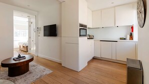 Une cuisine moderne avec des armoires blanches, un four encastré et un four à micro-ondes. On y trouve également un coin repas avec une table en bois et un tapis.