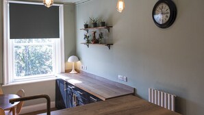 A kitchen with a wooden countertop, hanging light bulbs, a clock, and shelves with plants.