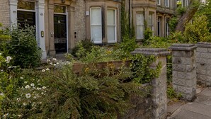 A row of terraced houses with numbered doors, a stone wall, and a garden with flowers.