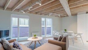 Una sala de estar moderna con un sofá grande, una mesita redonda y un comedor con sillas blancas.