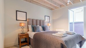 Un dormitorio con una cama grande, dos mesitas de noche con lámparas, una mesita auxiliar de madera y una ventana con vistas.