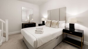 A hotel room with a large bed, two bedside tables, a mirror, and a nightstand. - Luxurious Serviced Apartments in the Heart of Marylebone, London (London)