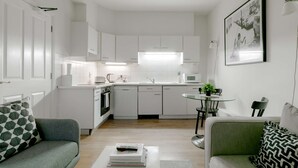 A modern kitchen with white cabinets, a microwave, and a sink. There is a dining area with a round table and chairs. - Luxurious Serviced Apartments in the Heart of Marylebone, London (London)