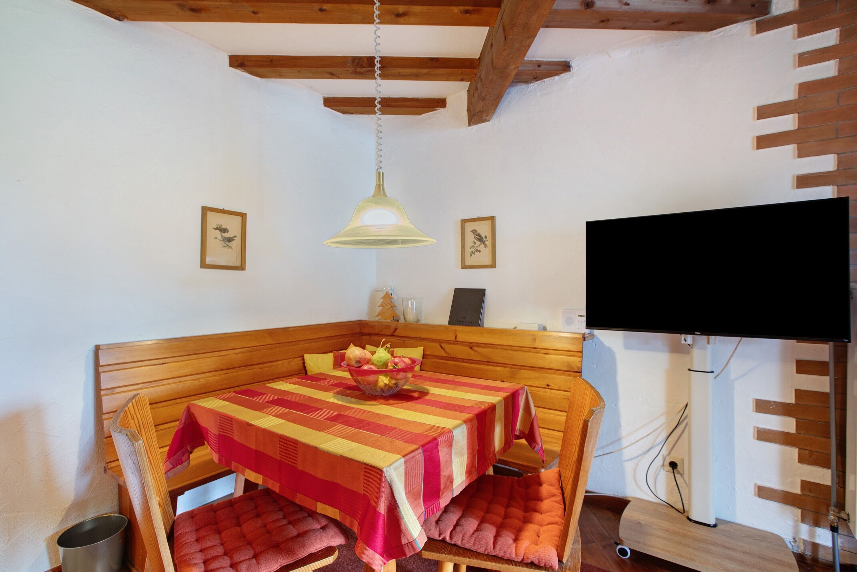 A dining area with a wooden table, red cushioned chairs, a fruit bowl, and a hanging light fixture.
