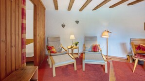 Une pièce avec des poutres en bois, deux fauteuils, une petite table avec une lampe et un lit doté d’un rideau.
