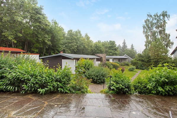 A residential area with stone pathways, lush greenery, and houses with varying roof styles.