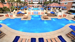 A large pool with multiple lounge areas, umbrellas, and a central water feature.