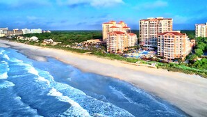 A beachfront hotel with multiple high-rise buildings, a sandy beach, and ocean waves.