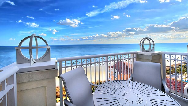 A balcony with a view of the ocean, featuring a table and chairs, and decorative metal elements.