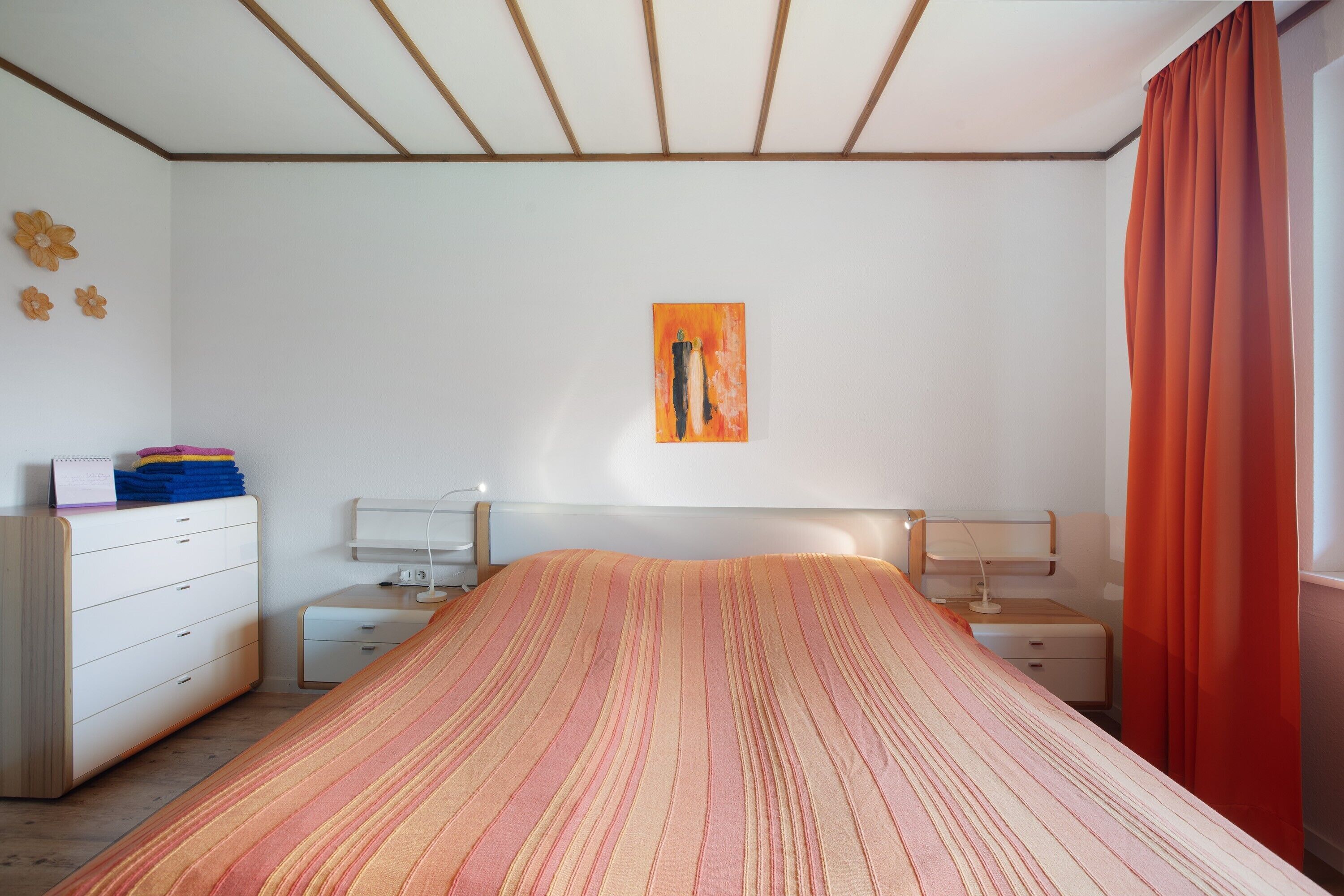 Een slaapkamer met een bed, nachtkastjes, een kaptafel, een schilderij aan de muur en een raam met gordijnen.