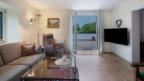 A living room with a sofa, armchair, glass coffee table, and a flat-screen TV. - Apartment 'Irene' with Mountain View, Private Terrace and Wi-Fi (Grafenhausen)