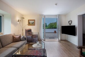 Una sala de estar con sofá, sillón, mesa de centro de vidrio y televisor de pantalla plana.