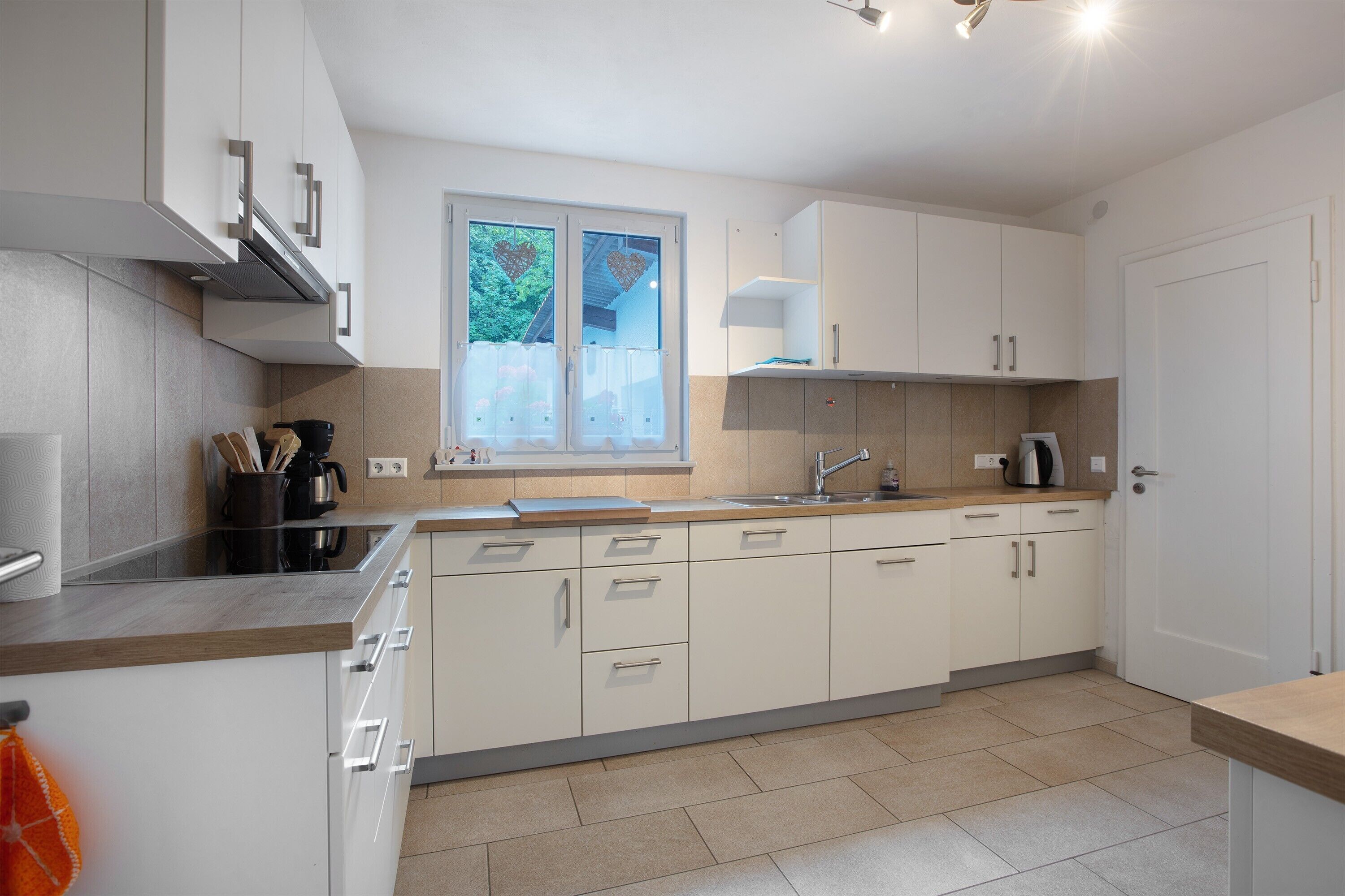 A modern kitchen with white cabinets, a stainless steel range hood, and a window with a view of greenery.