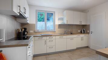 A modern kitchen with white cabinets, a stainless steel range hood, and a window with a view of greenery.