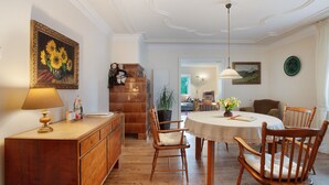 A dining area with a round table, wooden chairs, a lamp, and a painting of sunflowers. - Apartment 'Irene' with Mountain View, Private Terrace and Wi-Fi (Grafenhausen)