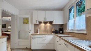 A modern kitchen with white cabinets, a stainless steel countertop, and a window with a view of greenery. - Apartment 'Irene' with Mountain View, Private Terrace and Wi-Fi (Grafenhausen)