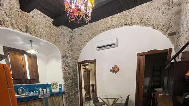 A room with a bed, a small table, and a chair. There is a chandelier hanging from the ceiling.