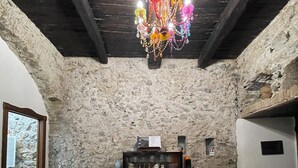 A rustic room with a stone wall, wooden ceiling beams, a patterned floor, a wooden cabinet, and a colorful chandelier.