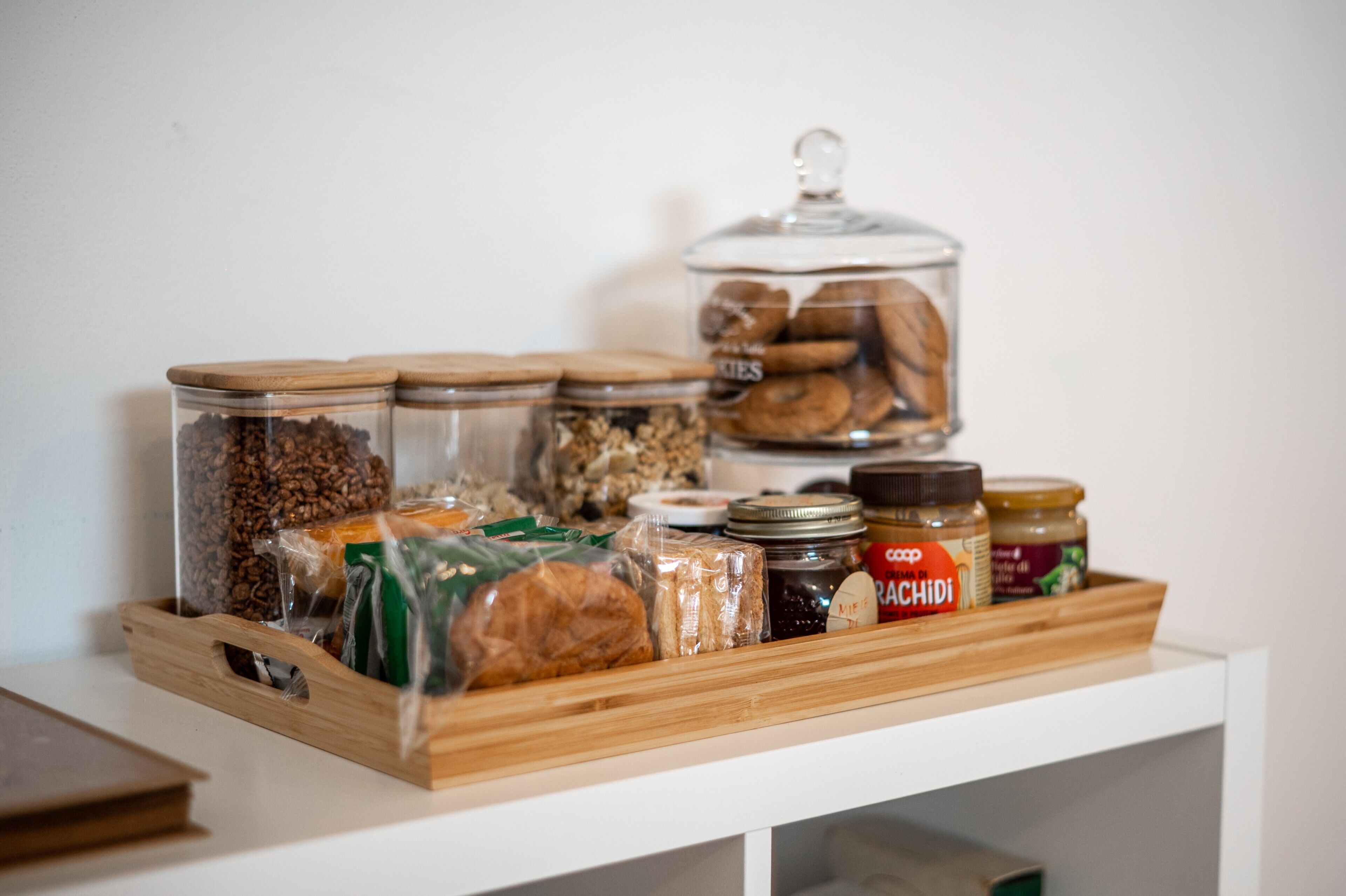 A wooden tray with various food items and jars on a white shelf.
