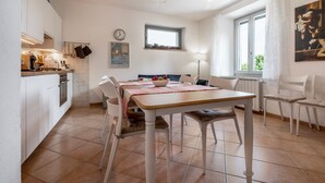 Une cuisine moderne avec des meubles blancs, une table à manger avec des chaises, un ventilateur de plafond et une fenêtre avec des rideaux.