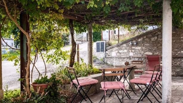 Une terrasse extérieure avec une pergola, une table, des chaises et un mur de pierre en arrière-plan.