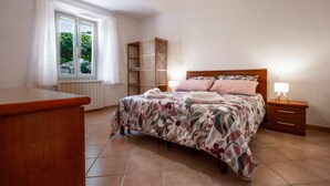 Une chambre à coucher comprenant un lit, des tables de chevet, une armoire, une fenêtre et un radiateur.