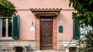 Un bâtiment avec une porte à deux battants de couleur marron, des volets verts et un banc en pierre devant.