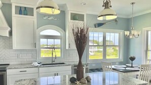 Une cuisine moderne avec des meubles blancs, un îlot en granit et des luminaires suspendus.