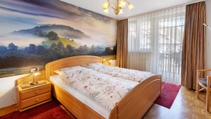 A bedroom with a large mural, a wooden bed, a nightstand with a lamp, and a chair. - Apartment 'Südschwarzwald' with Balcony and Wi-Fi (Bräunlingen)
