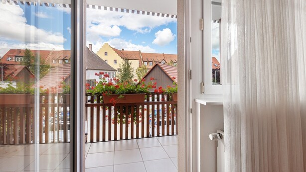 A balcony with a view of houses, a wooden fence, and a potted plant with red flowers. - Apartment 'Südschwarzwald' with Balcony and Wi-Fi (Bräunlingen)